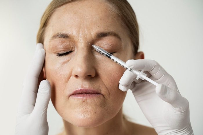 A person with closed eyes is receiving a Dysport injection on the forehead from someone wearing white gloves. The injector is holding the person's head steady with one hand while administering the injection with the other.