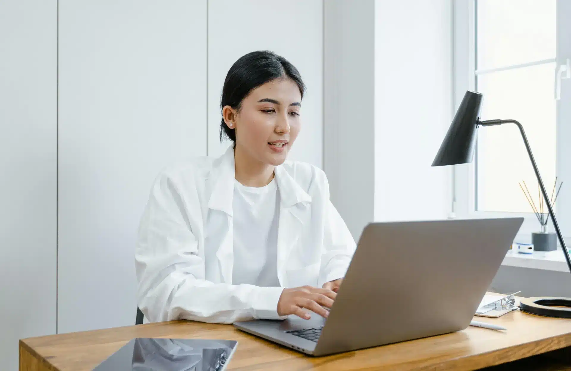 Medical professional in her office, typing on a laptop placed on her desk