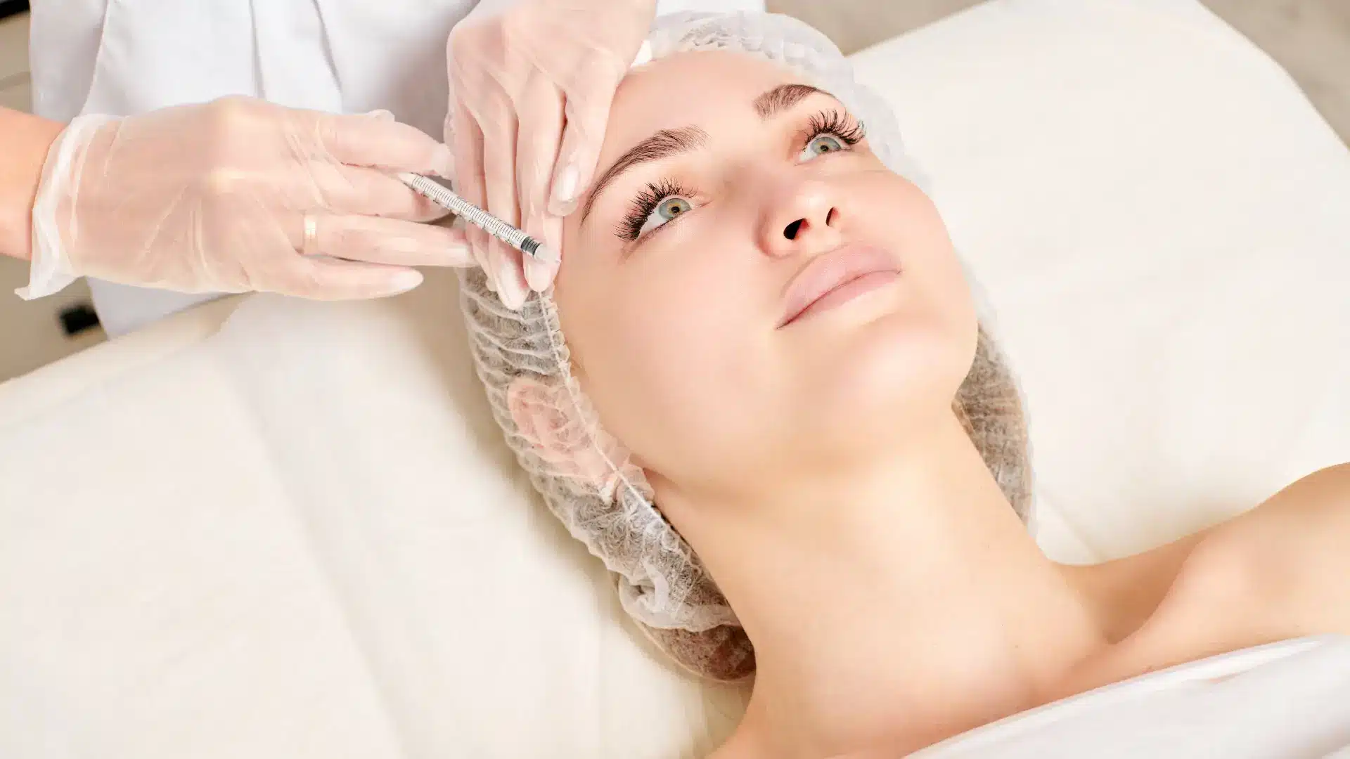 A healthcare professional administers injectable treatment to female patient laying down.