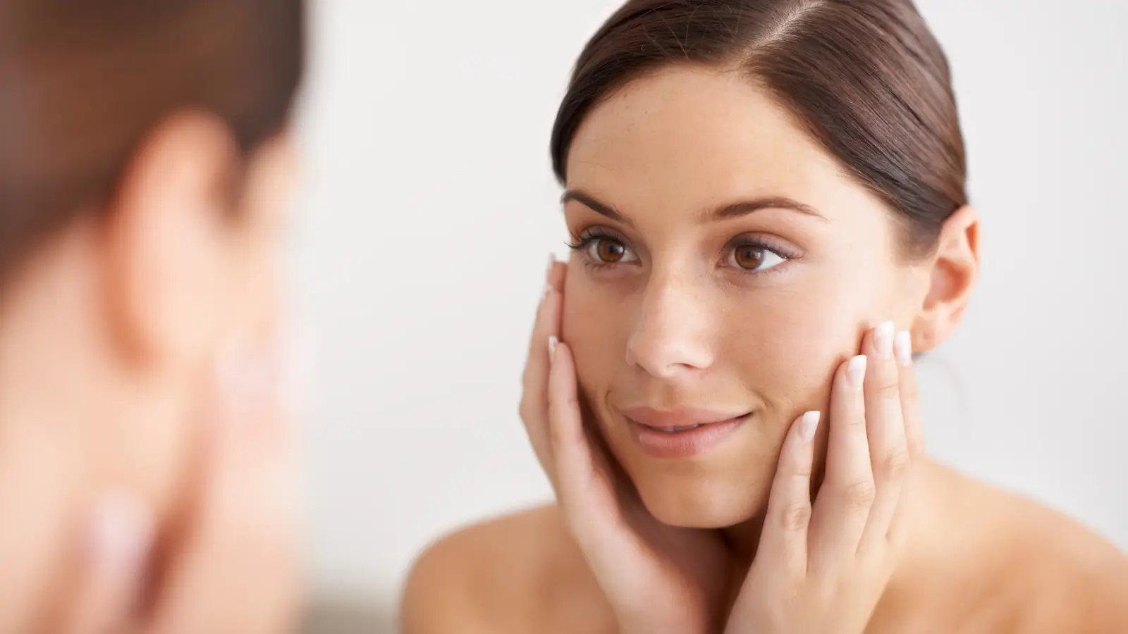 Woman admiring her glowing skin in the mirror.